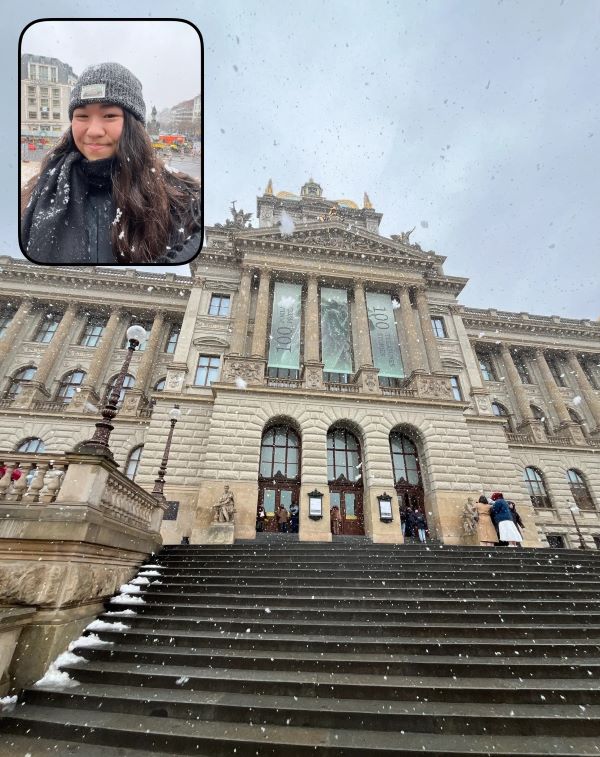 A study abroad student shown in an small window smiling at the camera, with a large building in the forefront of the frame