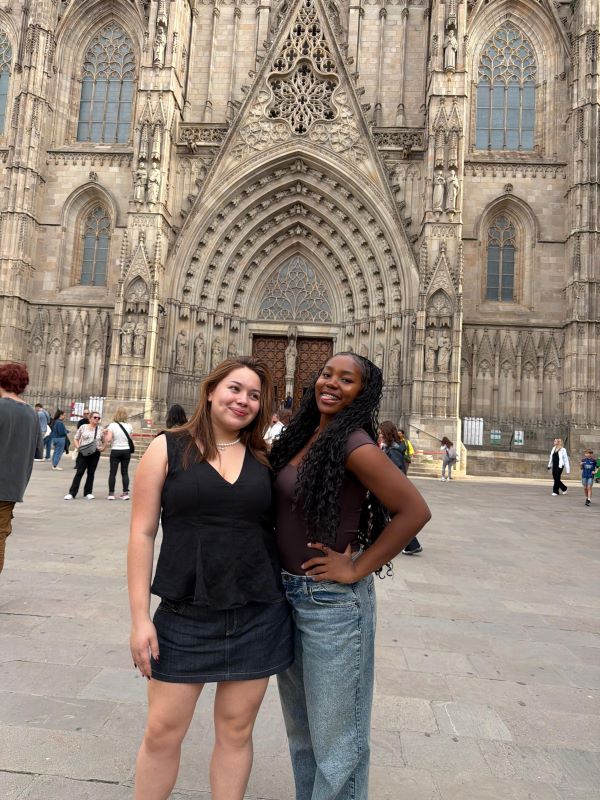 Two study abroad students standing outdoors in front of a large ornate building and smiling at the camera