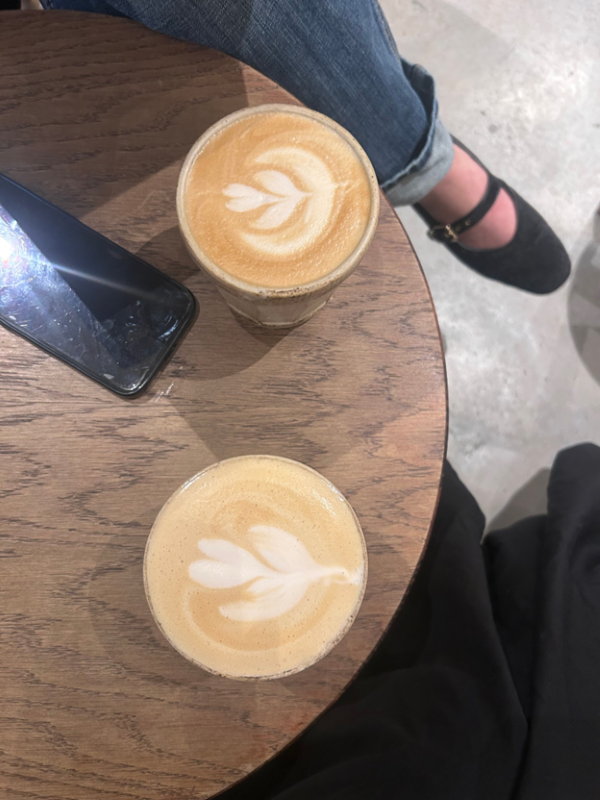 Two cups of coffee with intricate foam designs as seen from above sitting on a wooden table indoors