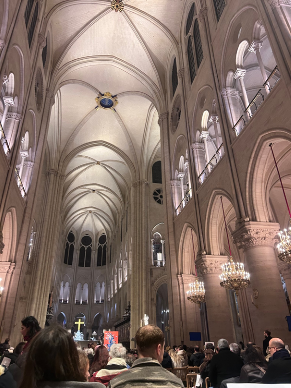 The interior of a massive cathedral, with tall white walls and ceilings and many people sitting in pews in front of the altar