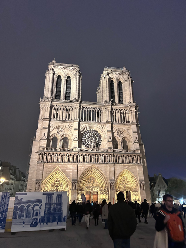 Many people walking around outside a tall ornately decorated building as seen at night