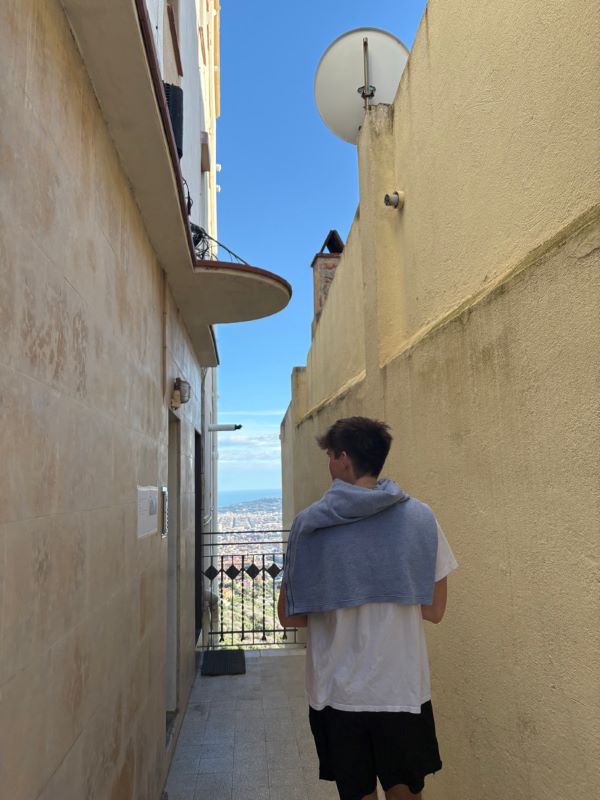 A study abroad student with their back to the camera standing between two sand-colored walls looking out at a scenic view in the distance