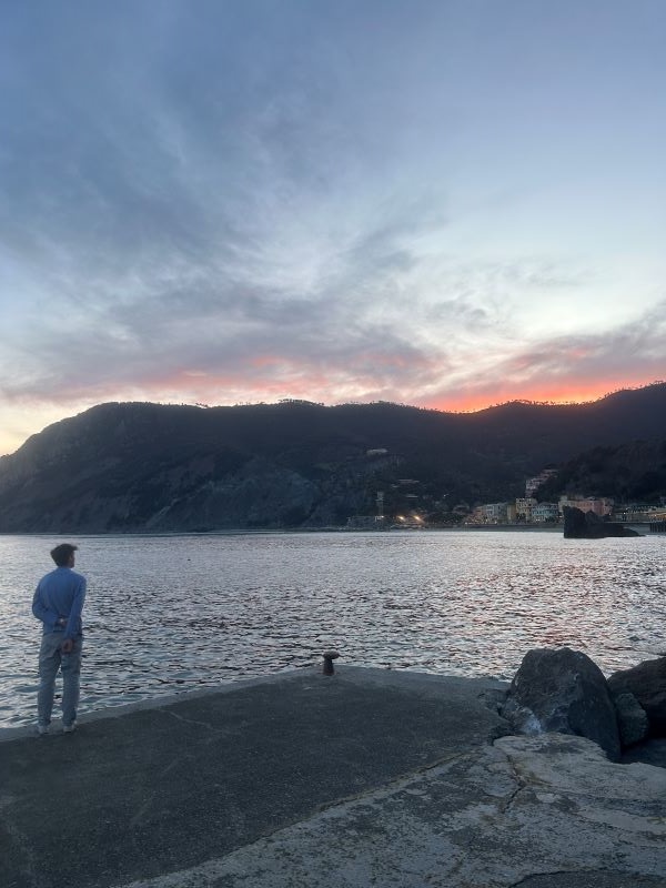 A study abroad student standing by a body of water in low light with their back turned to the camera