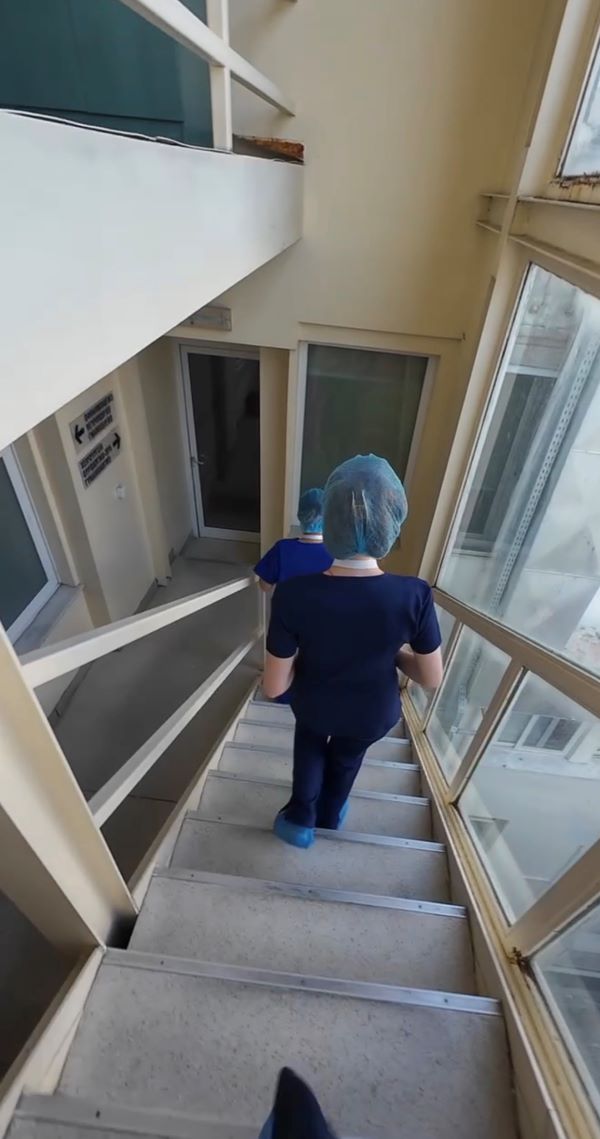 Two pre-med shadowing students as seen from behind wearing blue scrubs while walking down an indoor staircase