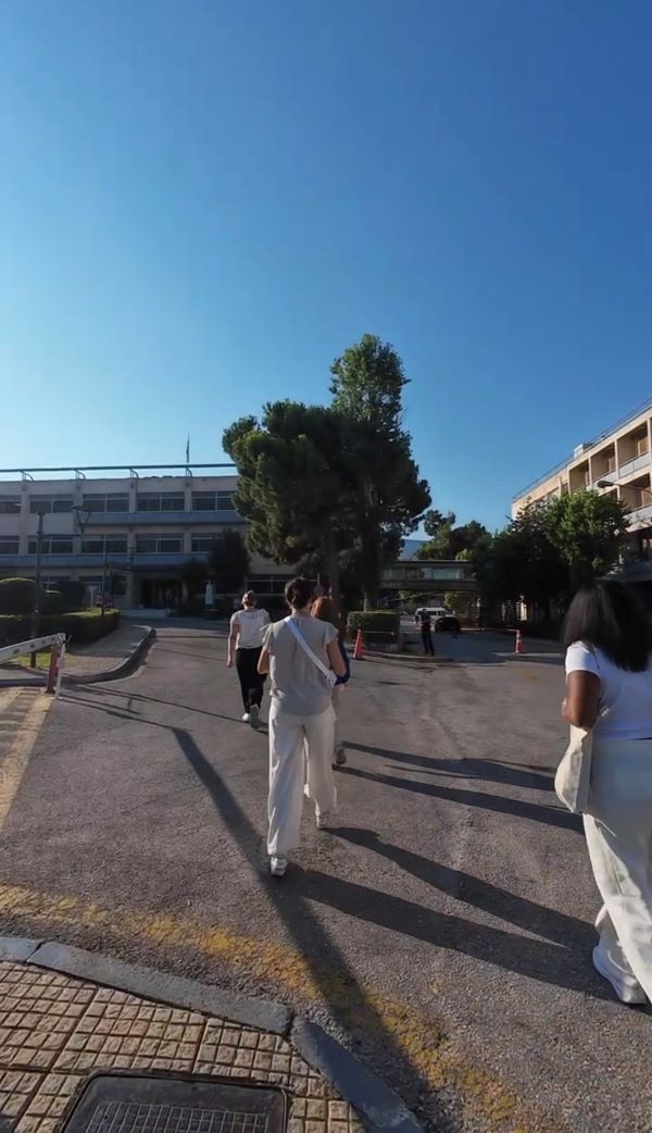 Several pre-med shadowing students as seen from behind walking outdoors through a parking lot toward a nondescript building
