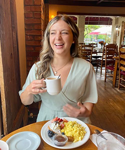A person sitting at a table with a plate of food and a coffee mug