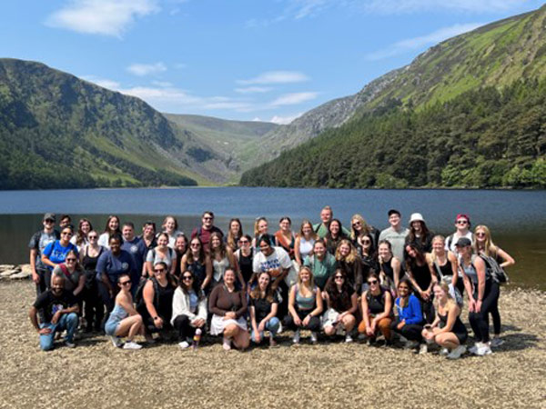a group of study abroad students posing for a photo in front of water and mountains