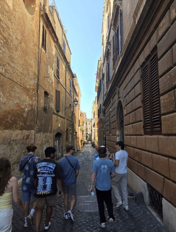 A group of study abroad students as seen from behind walking down a narrow cobblestone city street