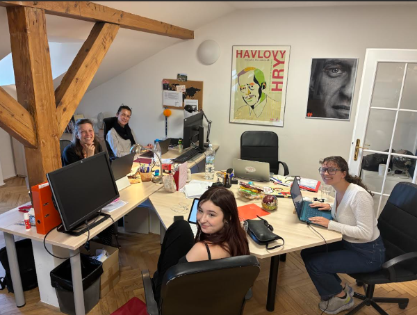 Four people sitting at desks indoors and smiling at the camera