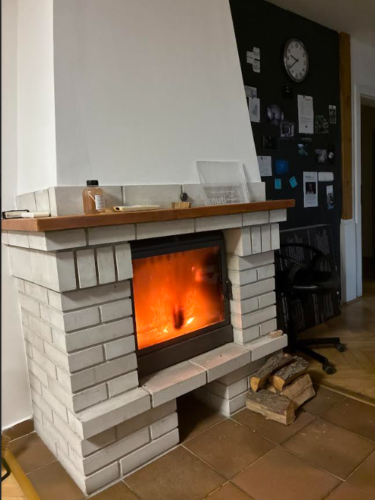 A small indoor fireplace made of gray stone and featuring a small blazing orange fire