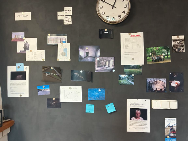 A gray indoor wall featuring photos, documents, and sticky notes held up by small round magnets