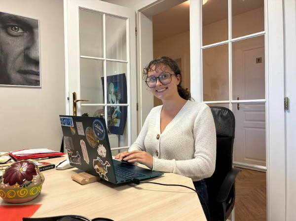 A study abroad student sitting at a table indoors in front of a laptop and smiling at the camera