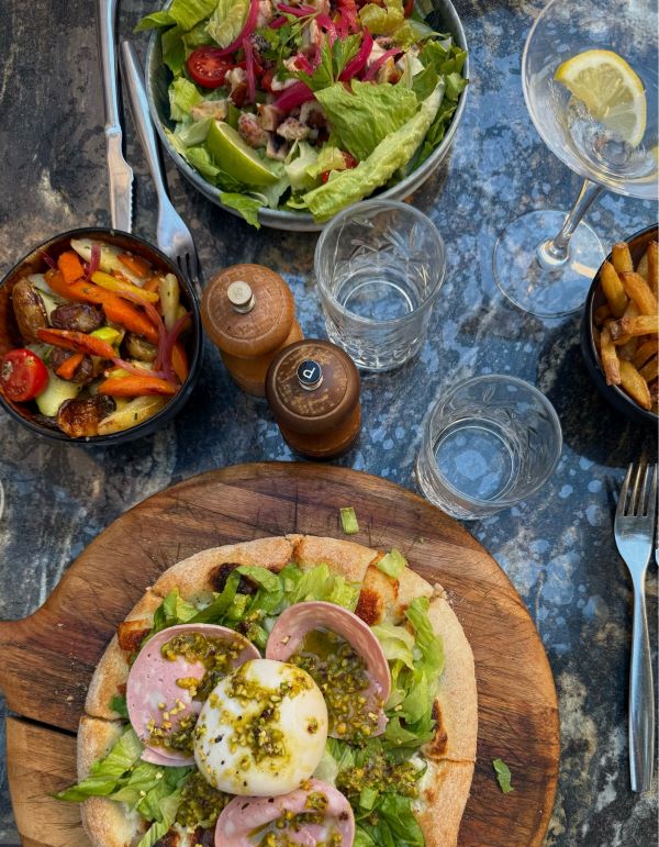 Plates of food and glasses of water laid out on a table, including a small pizza and a green leafy salad