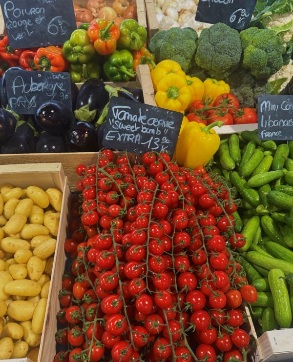 Boxes of brightly-colored produce at a market stall, featuring small bright red tomatoes front and center
