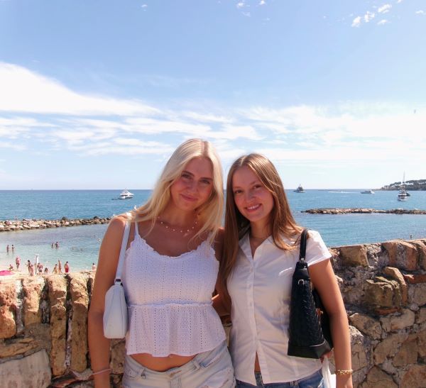 Two study abroad students standing in front of a large body of water and smiling at the camera