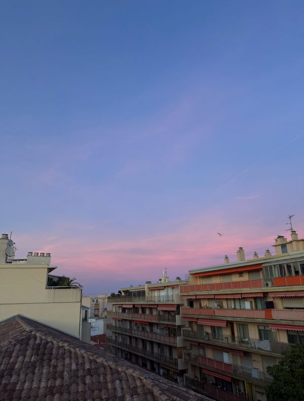 A pink, purple, and blue sunset seen from several stories up and with tan apartment buildings in the foreground
