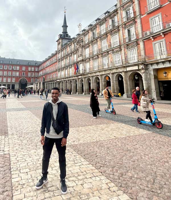A study abroad student standing in a plaza with Plaza Mayor, Madrid in the background