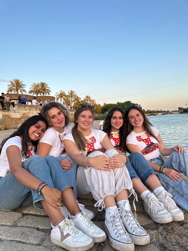 A group of study abroad students sitting on a stone surface near body of water