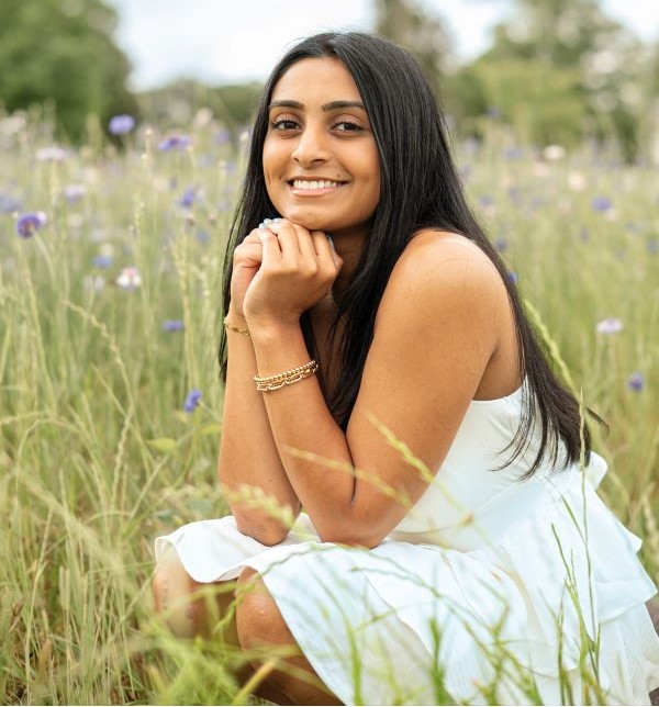 A study abroad student smiling at the camera while crouched down in a field of tall grass with their hands resting under their chin