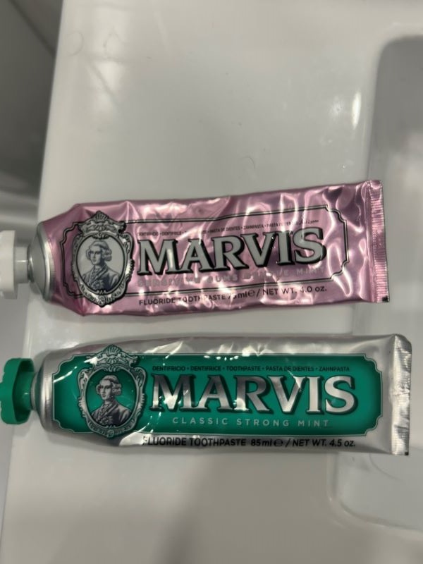 A pink and a green tube of toothpaste laid on a counter, each featuring the word