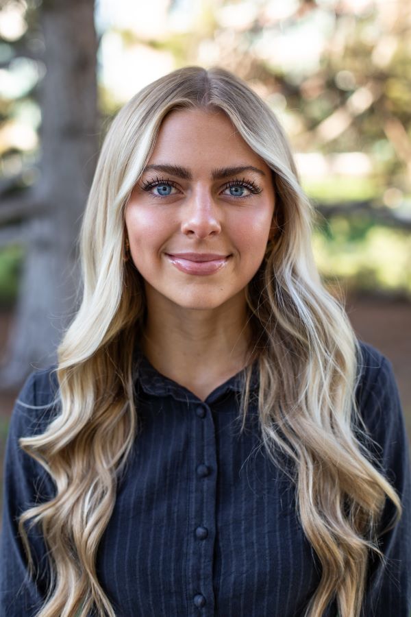 A study abroad student with long blonde wavy hair and wearing a dark blue shirt smiling at the camera