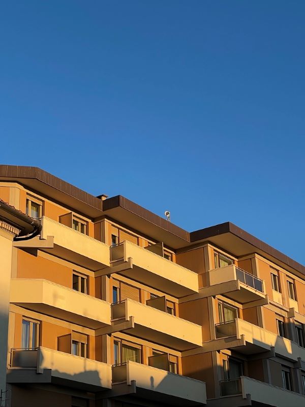 Tall uniform tan buildings with wide balconies bathed in golden evening light underneath a clear blue sky