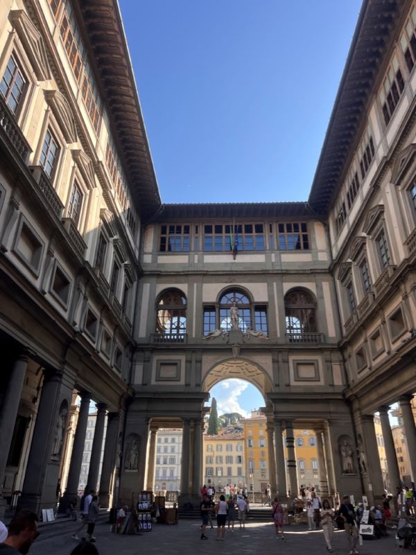 People walking throughout the interior of an outdoor courtyard with tall walls intricately carved with statues and windows