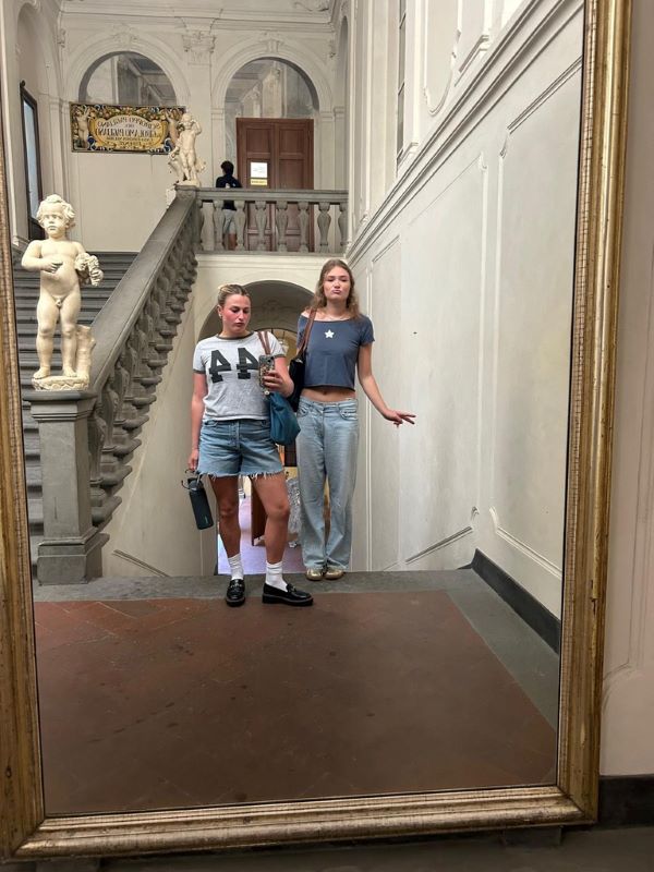 Two study abroad students as seen reflected while taking a selfie in a large indoor mirror