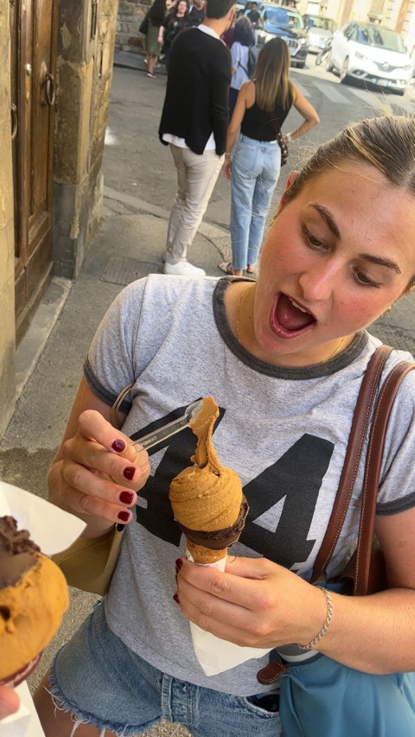 A study abroad student holding an ice-cream cone with two scoops of gelato, looking down at it with a happy look on their face