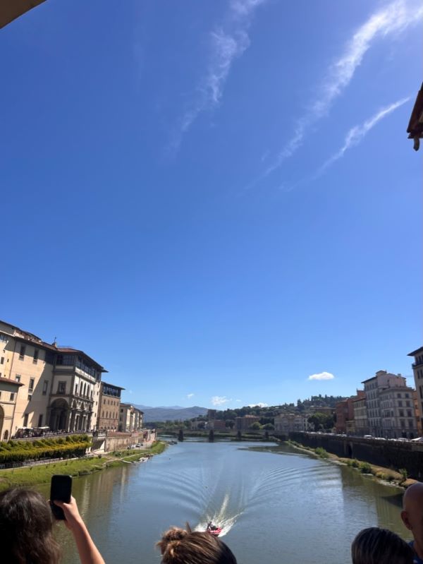 A view from above of a river underneath a bright blue sky and hemmed in on each side by sand-colored buildings