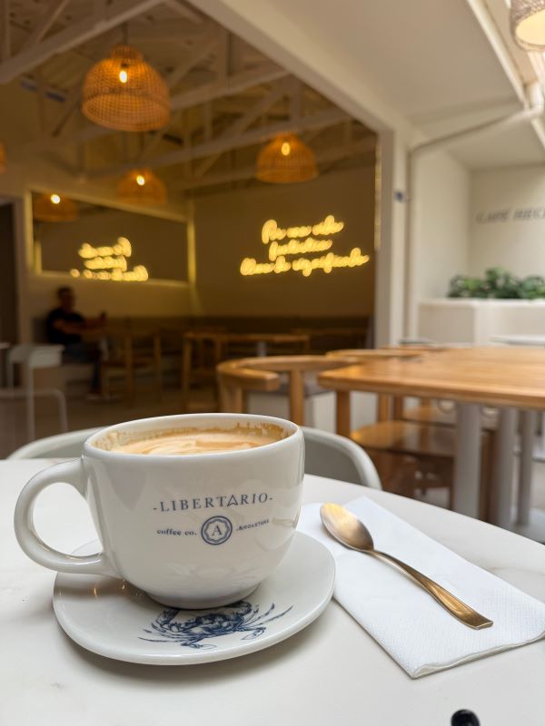 A large cup of coffee in a white cup sat on a white table next to a spoon on a napkin in an indoor setting