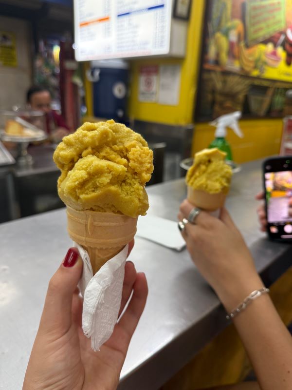 Two hands seen each holding a cone with yellow-orange-colored scoop of ice cream