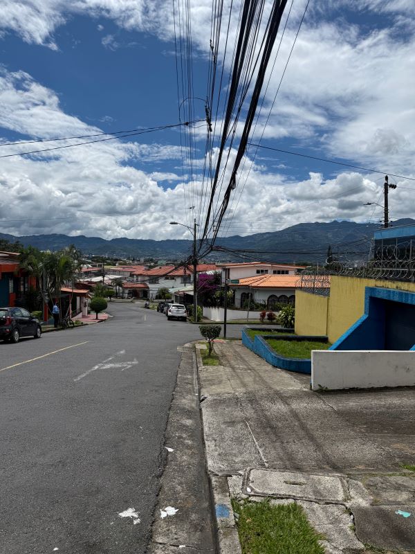 A view of a road leading to low-lying city buildings from a slight height with mountains in the background under a blue sky