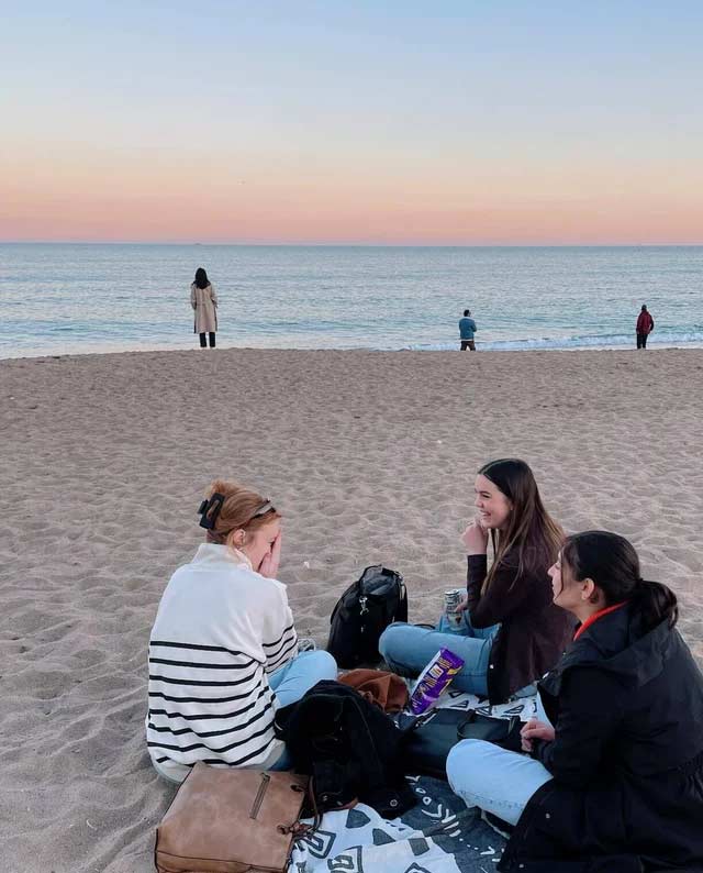 Three friends sitting on a beach during sunset in Barcelona, Spain