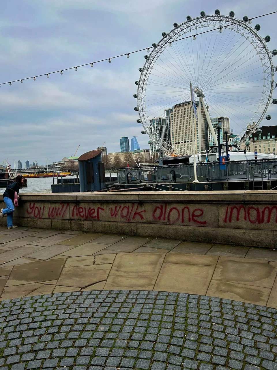 A graffiti quote saying, "You will never walk alone", with the London Eye in the back