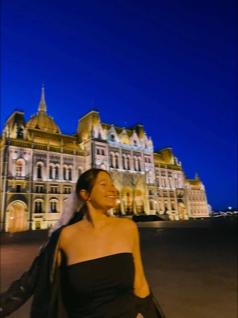 A student smiling and standing in front of the lit up Parliament Building in Budapest, Hungary