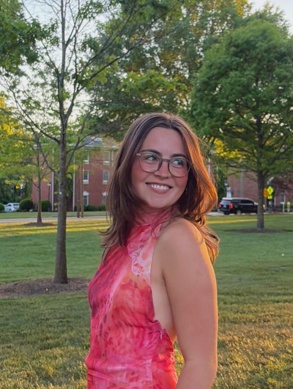 A study abroad student in an outdoor setting wearing a pink shirt smiling while looking away from the camera