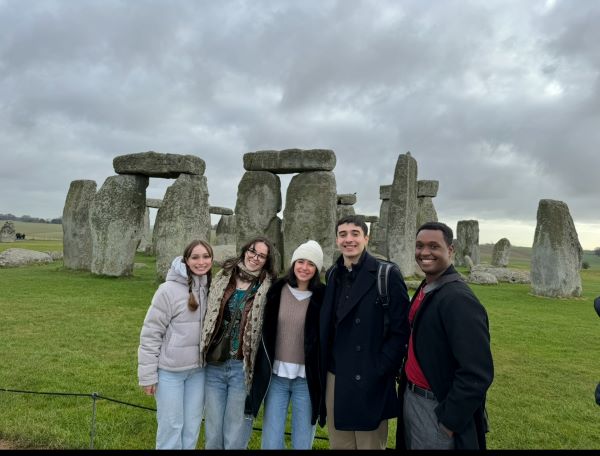 Five study abroad students standing outdoors and smiling at the camera in front of a large ancient collection of stones