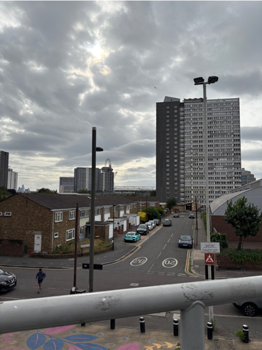 A view from above of a city street under a gray cloudy sky with tall buildings in the distance
