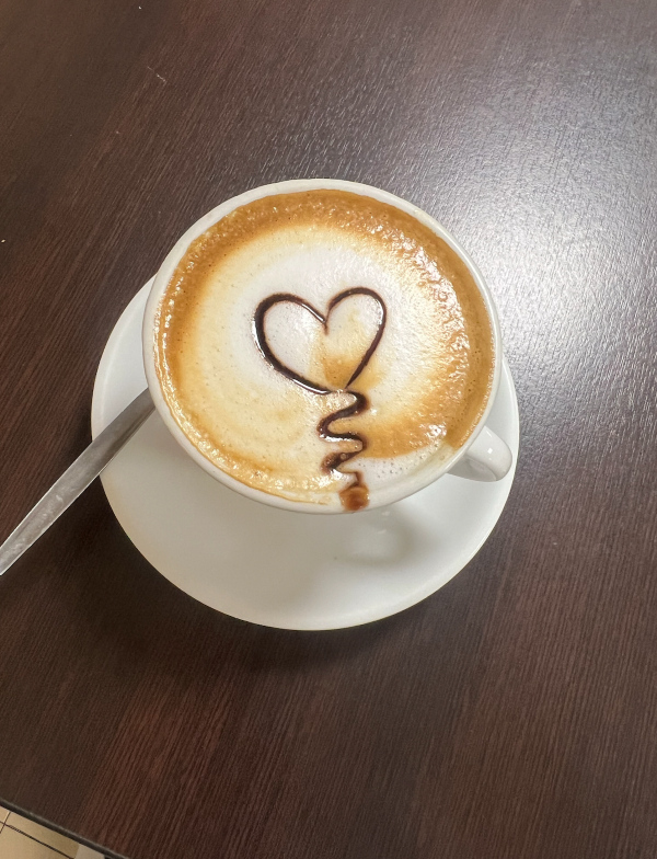 A white mug of coffee with a brown and cream foamy top and a heart drawn on it sitting on a table