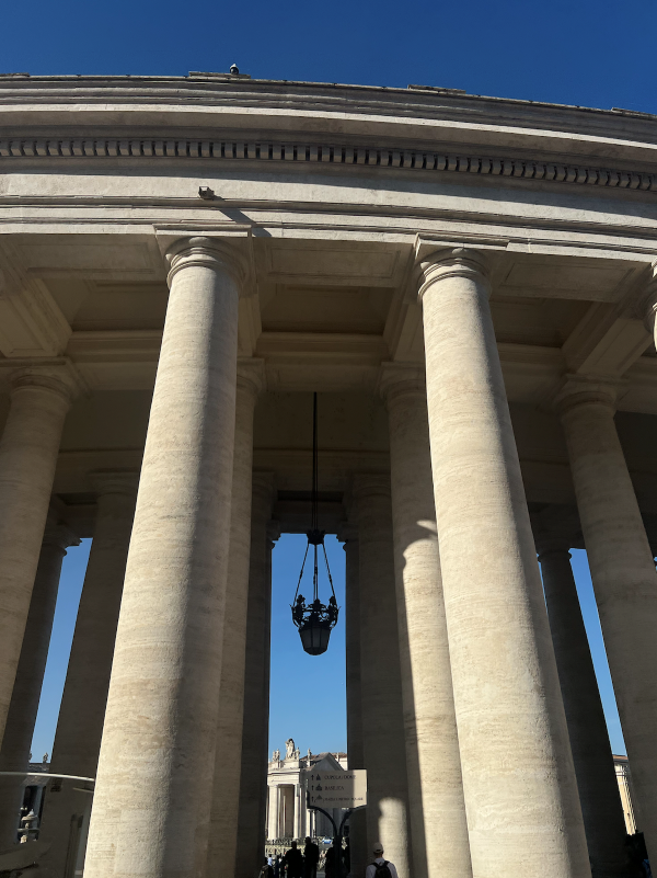 A tall stone building held up by multiple rows of columns seen from below underneath a bright blue sky
