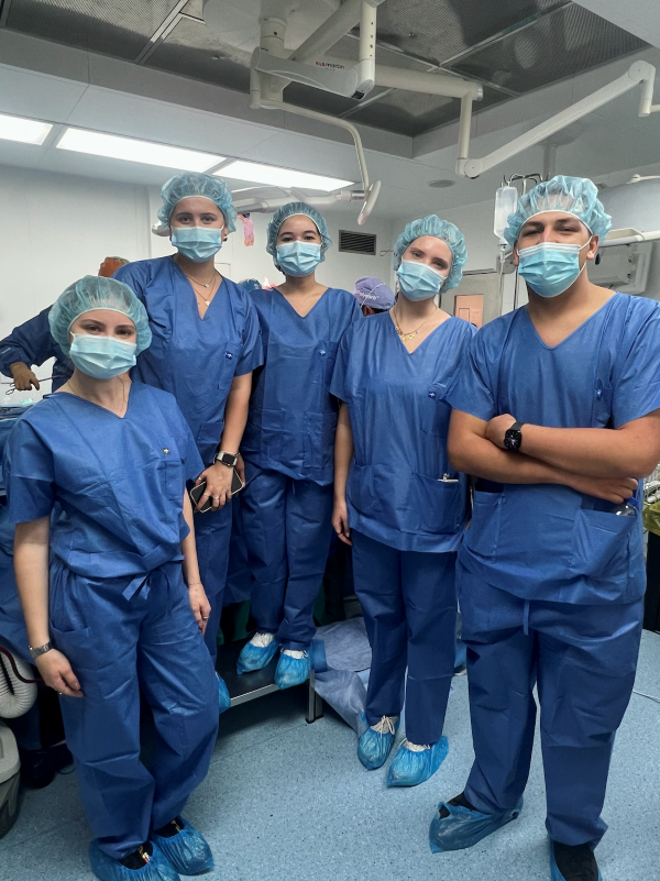 Five study abroad students standing together, wearing blue scrubs and disposable face and hair masks while smiling at the camera