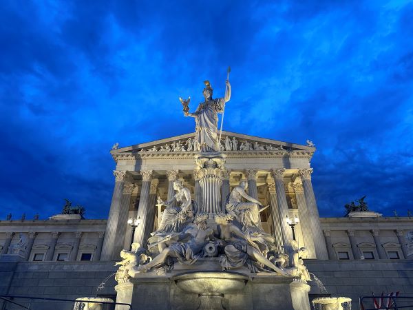 A large stone building with an intricate facade featuring various statues lit up and seen from below under an electric blue evening sky