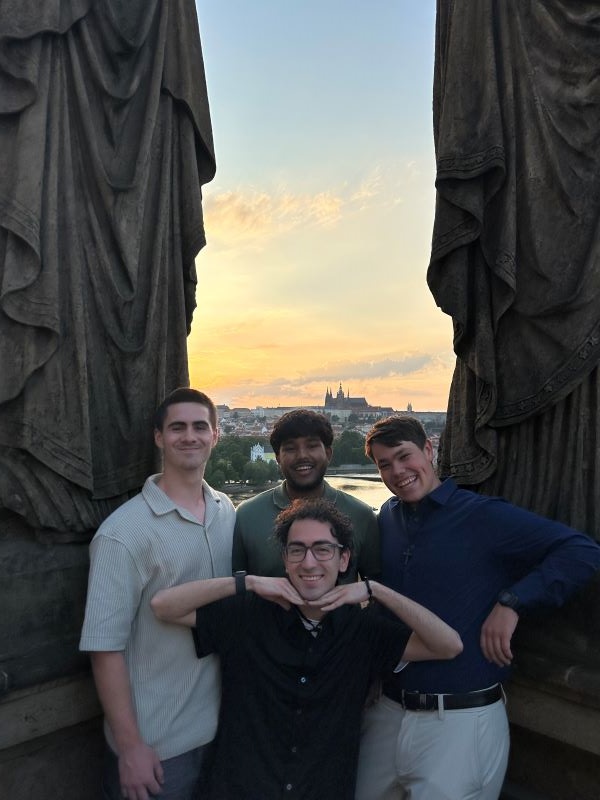 Four study abroad students standing together and smiling at the camera with a collection of city buildings lit by sunset in the background