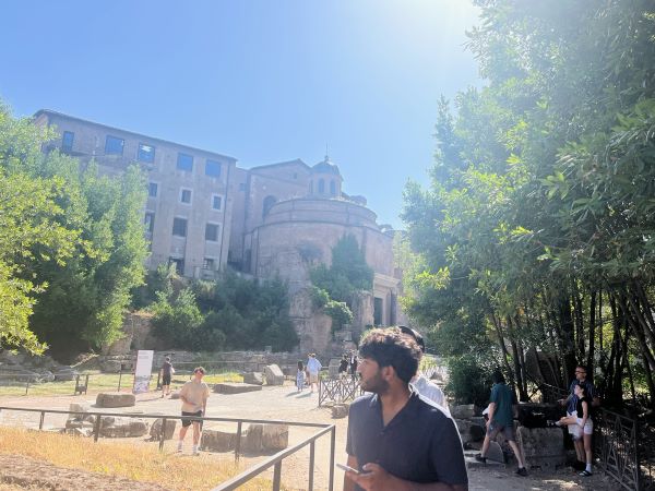 A study abroad student looking to their right away from the camera in front of a large old stone building