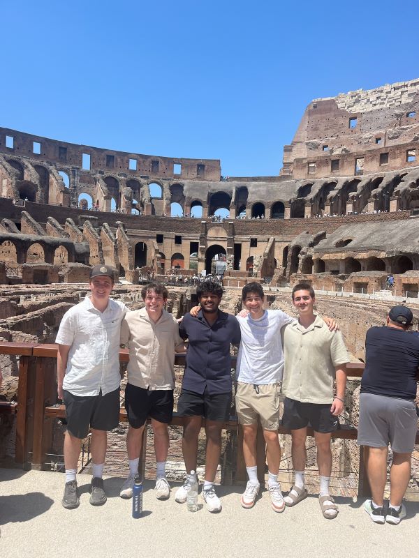 Five study abroad students standing outdoors in a large open-air building with many people walking around in the background