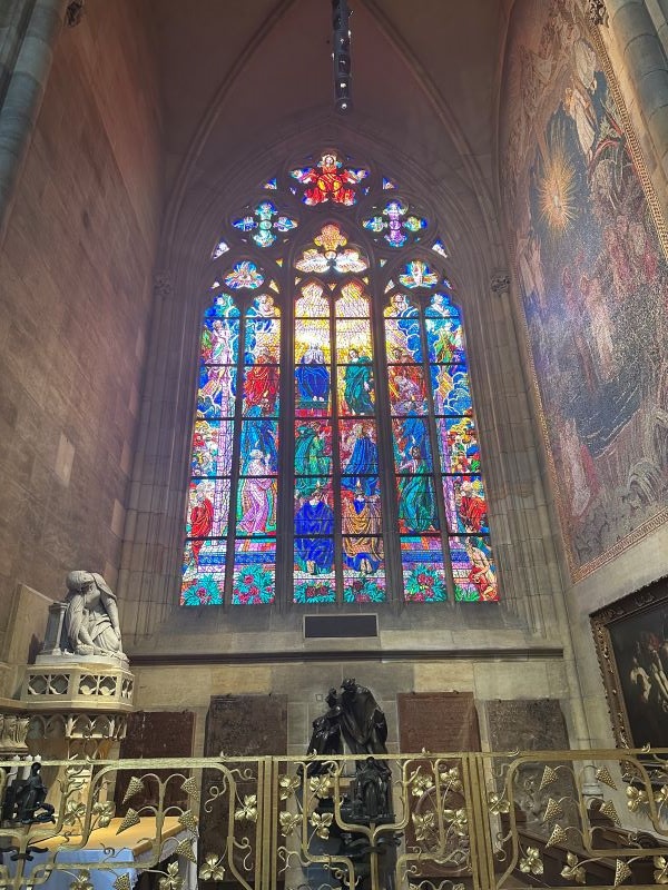 A large colorful stained-glass window featuring images of various religious figures, seen from inside a tall stone building,