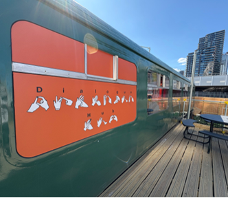 The exterior of a green train with an orange sign on it showing images of various letters signed in British Sign Language