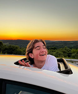 A person in a car with a sunset in the background