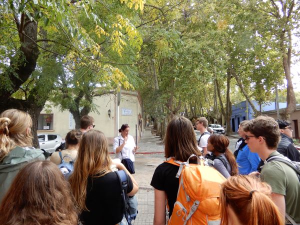 A group of study abroad students facing away from the camera toward a person in a white shirt in the middle of the frame